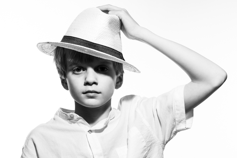 A young boy holds onto his hat as he is photographed in a buttondown Zara shirt.