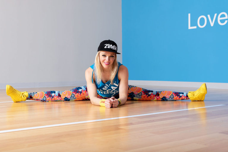 Colorful fitness photograph of a Zumba instructor doing the splits in a studio with "Love" painted on the wall.
