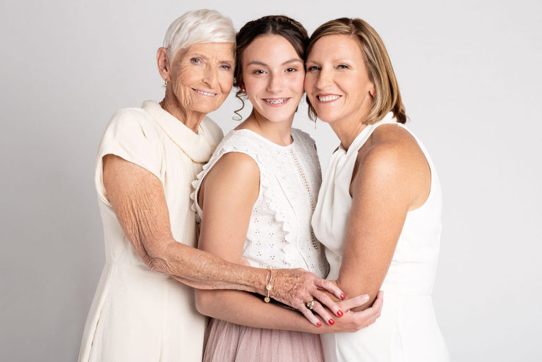 Grandmother and mother embrace each other and granddaughter during their styled photo session.