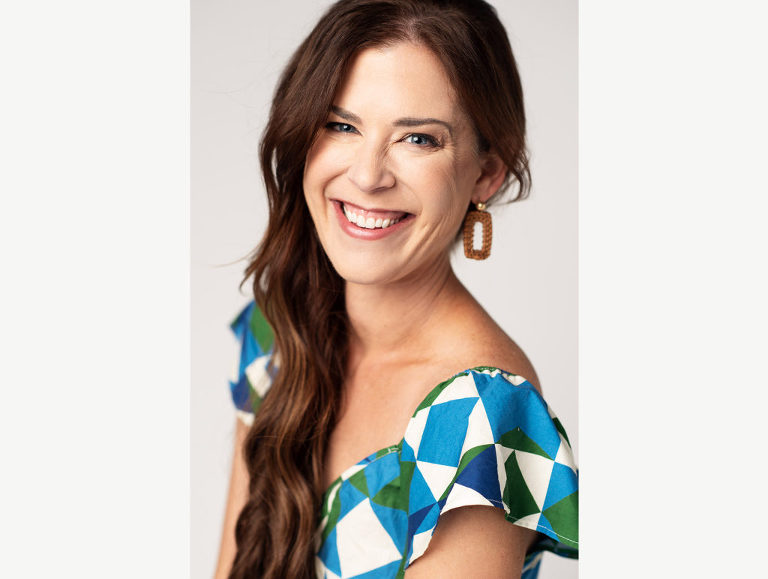 A woman smiles big as she makes eye contact with the viewer during her photo session.