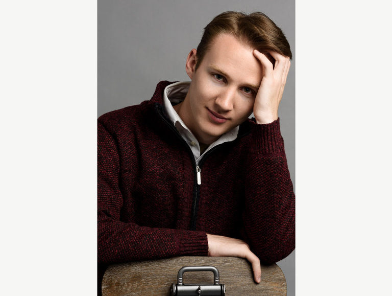 Editorial style photograph of a high school senior guy who leans on the back of his chair, resting his forehead in his hand.