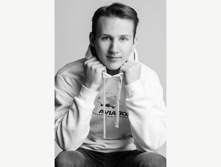 Editorial style photo of a high school senior guy holding the hood of his sweatshirt as he engages with the viewer.