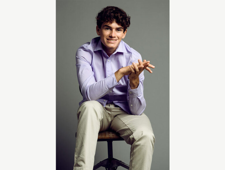 Relaxed look for a high school senior boy who leans forward and rubs his hands as he smiles at the viewer.