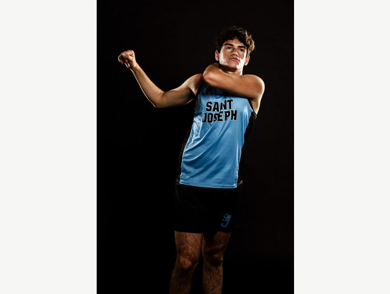 Candid portrait of a cross country runner stretching his shoulder during his senior photo session.