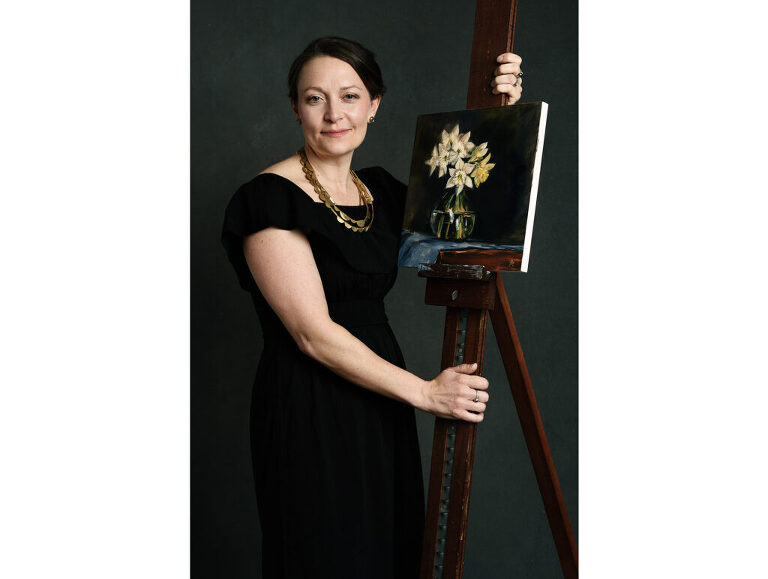 An artist poses for her portrait with one of her paintings.