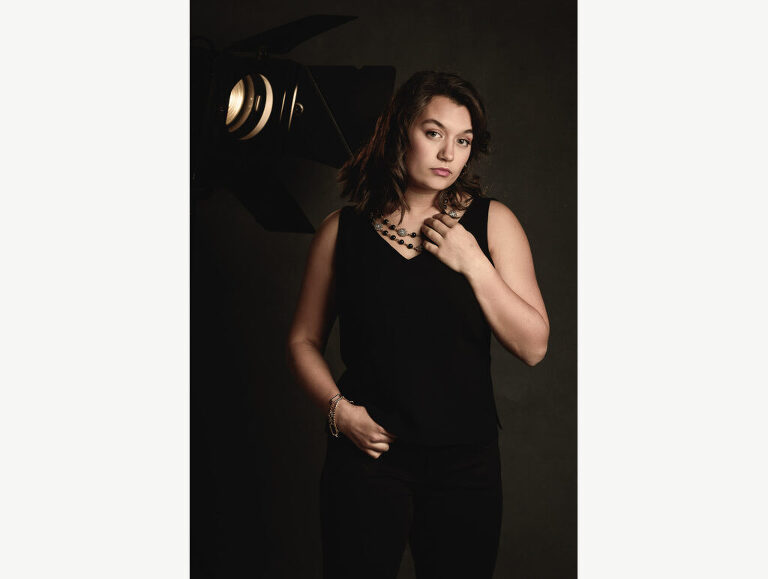 A high school senior girl with a love of performing poses with an old fresnel light during her photo session in studio.