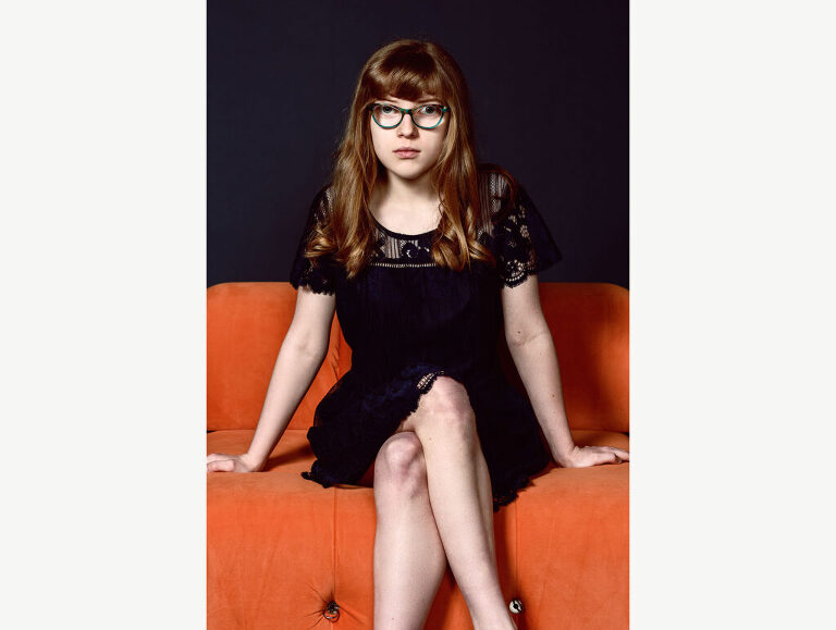 Serious studio photograph of a tween girl, looking serious in her glasses.