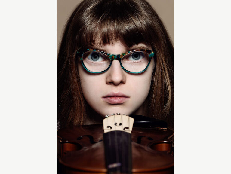 Studio photograph of a preteen girl resting her chin on the end of her violin.