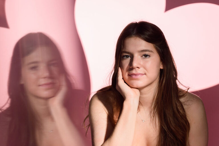 Portrait of a high school senior girl with a pink heart in the background.