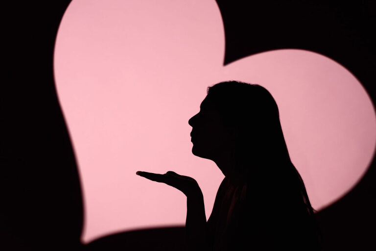 Silhouette of a high school senior girl blowing a kiss on a background featuring a pink heart.