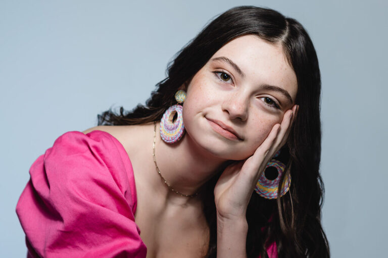 Portrait of a teenage girl who rests her face in her hand as she engages with the camera.